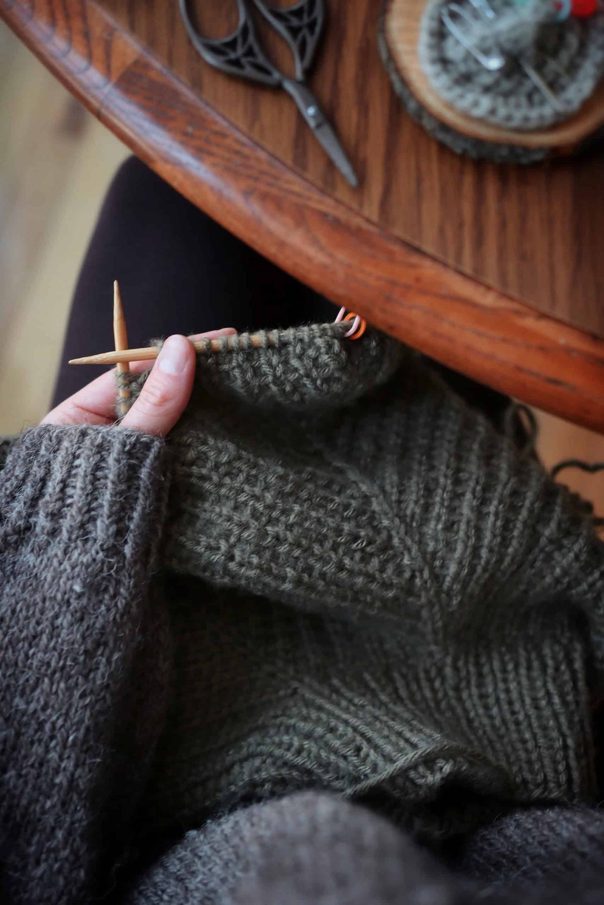 Hands knitting cream colored raglan sweater with wooden needles showing top-down construction technique