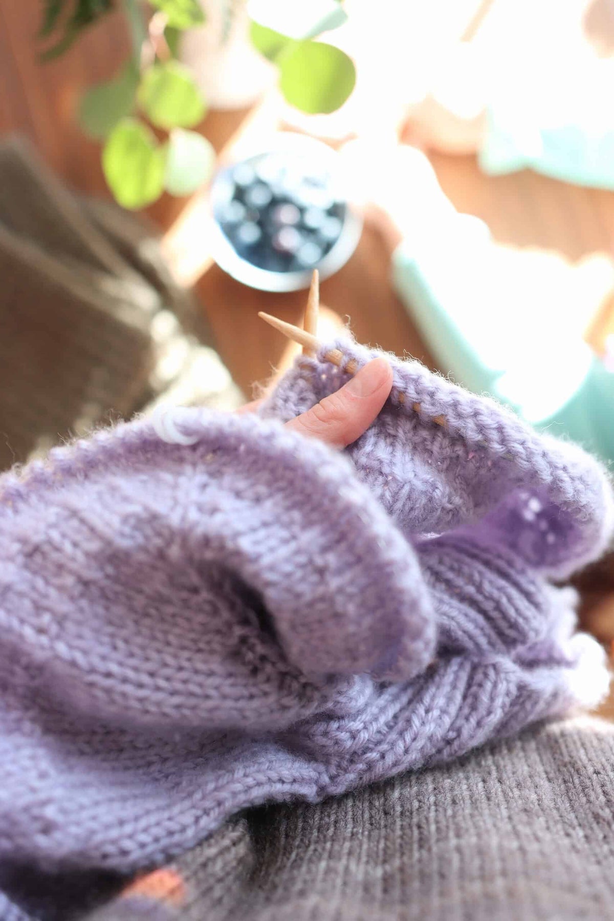 Purple yarn skein with knitting needles and partially knitted sweater fabric showing stockinette stitch texture