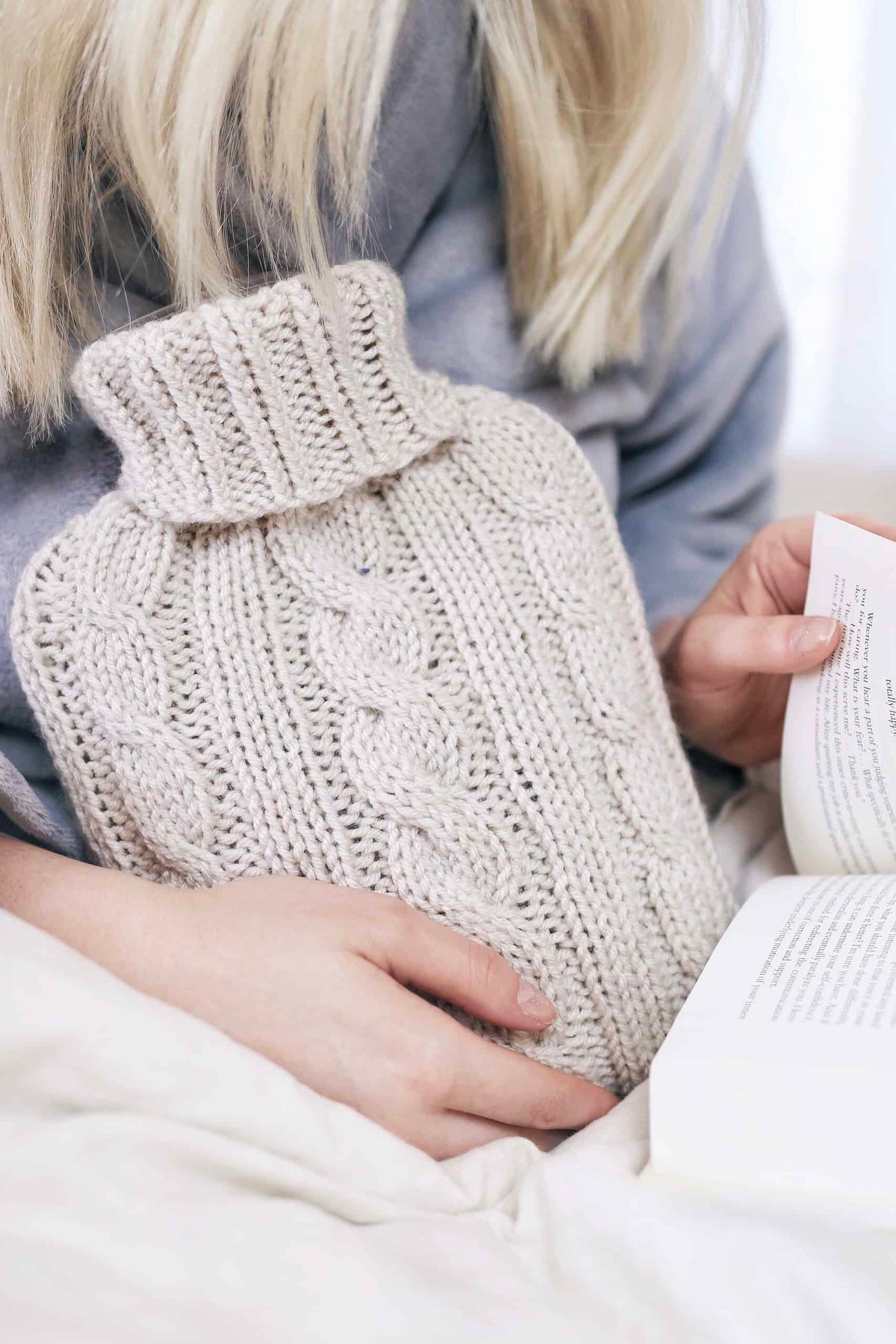 Cream cable knit hot water bottle cozy with flowing vintage-inspired design on white bedding