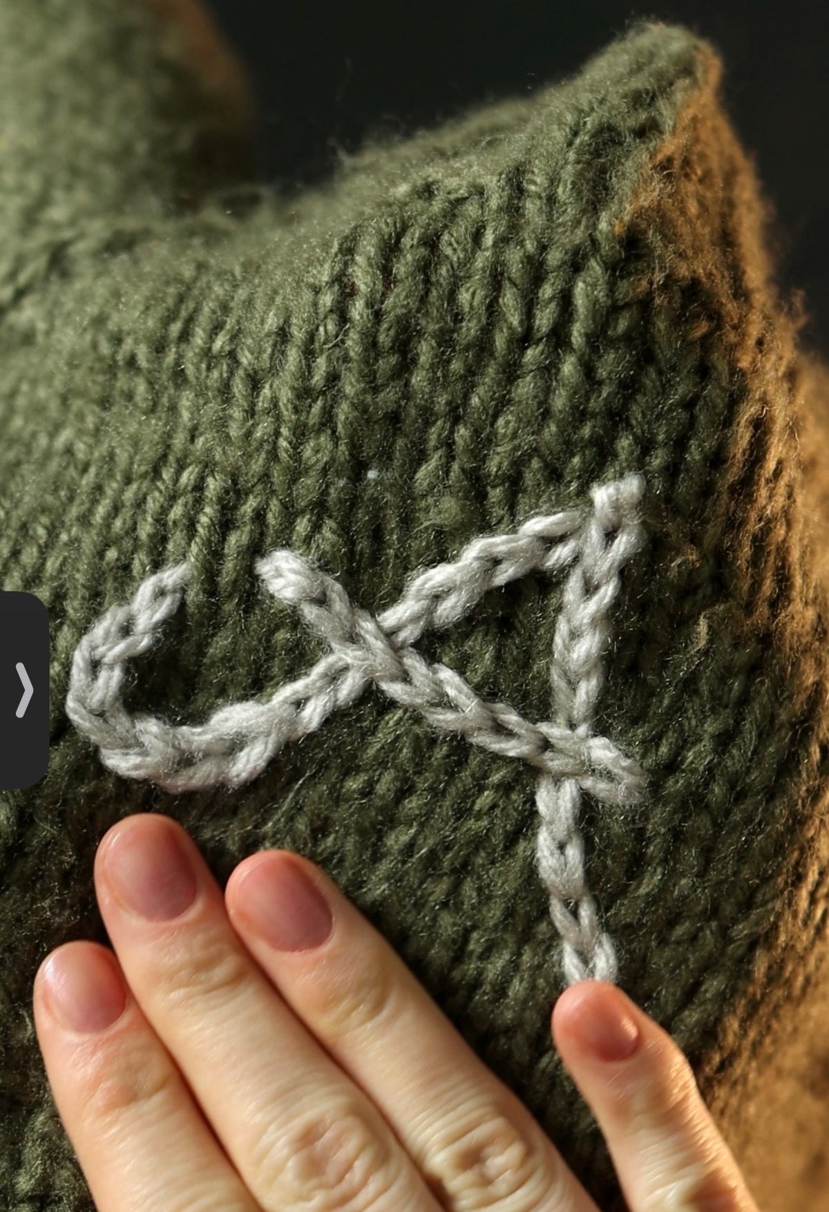 Close-up of hands working surface crochet embellishment on knitted fabric with crochet hook and yarn