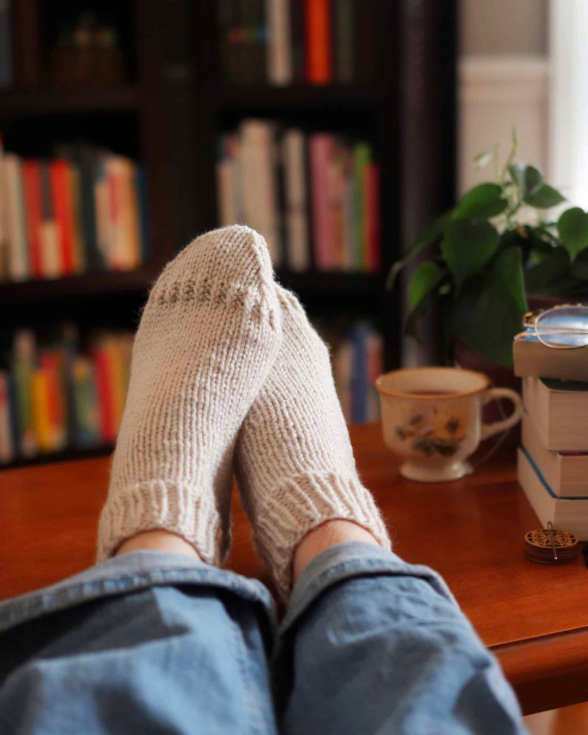 Knitted ankle socks in cream worsted yarn on wooden floor - Storytime Socks beginner-friendly pattern by Darling Jadore
