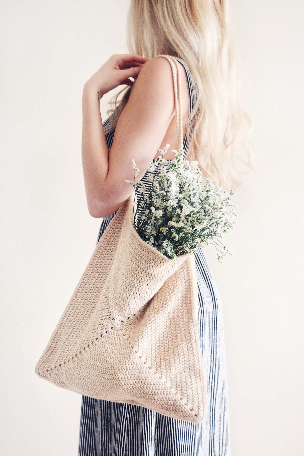 Beige crochet market tote bag with eyelet detail and wooden handles on neutral background