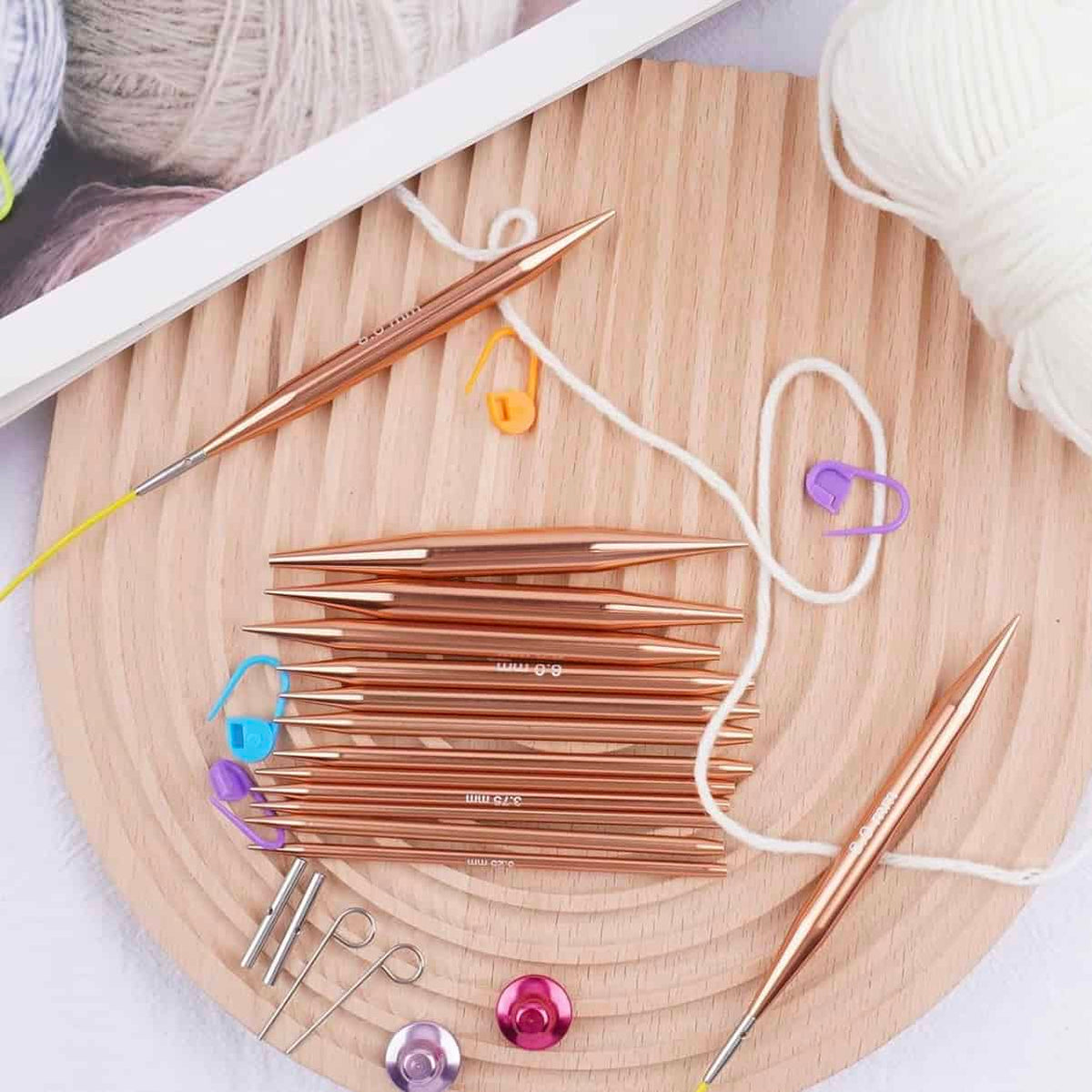 Rose gold interchangeable knitting needles with metal tips and cables arranged on white surface