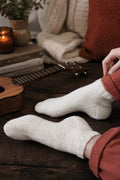 Classic ankle socks knitting pattern in natural cream yarn on wooden surface