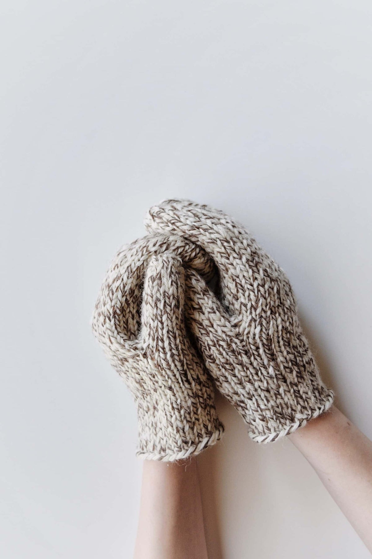Hand wearing cream knit mittens with ribbed cuffs - beginner friendly mittens knitting pattern