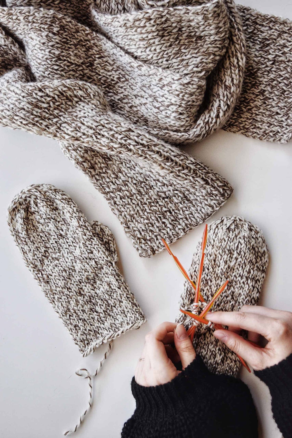 Cream knitted mittens with ribbed cuffs laid flat on white surface - Nora Mittens knitting pattern by Darling Jadore