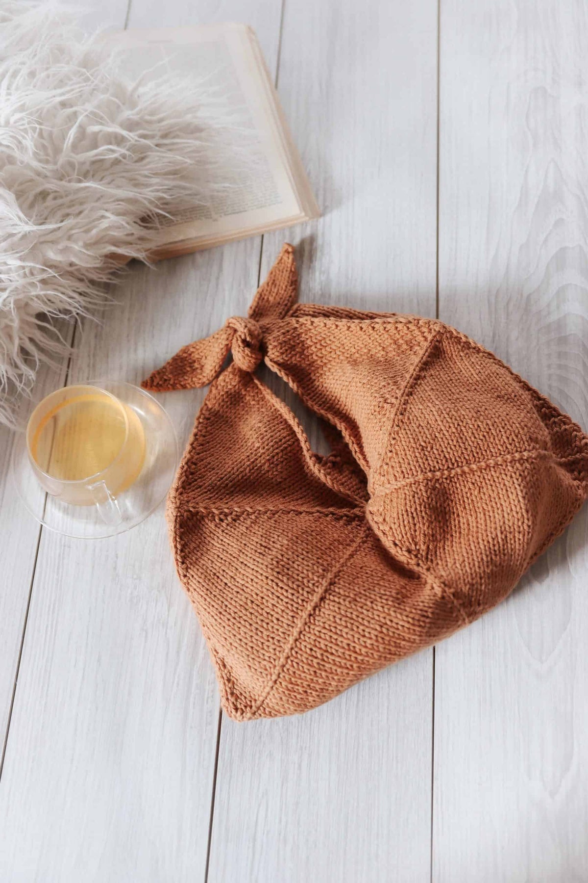 Cream knitted bento bag with knot-tie closure held by model wearing neutral sweater