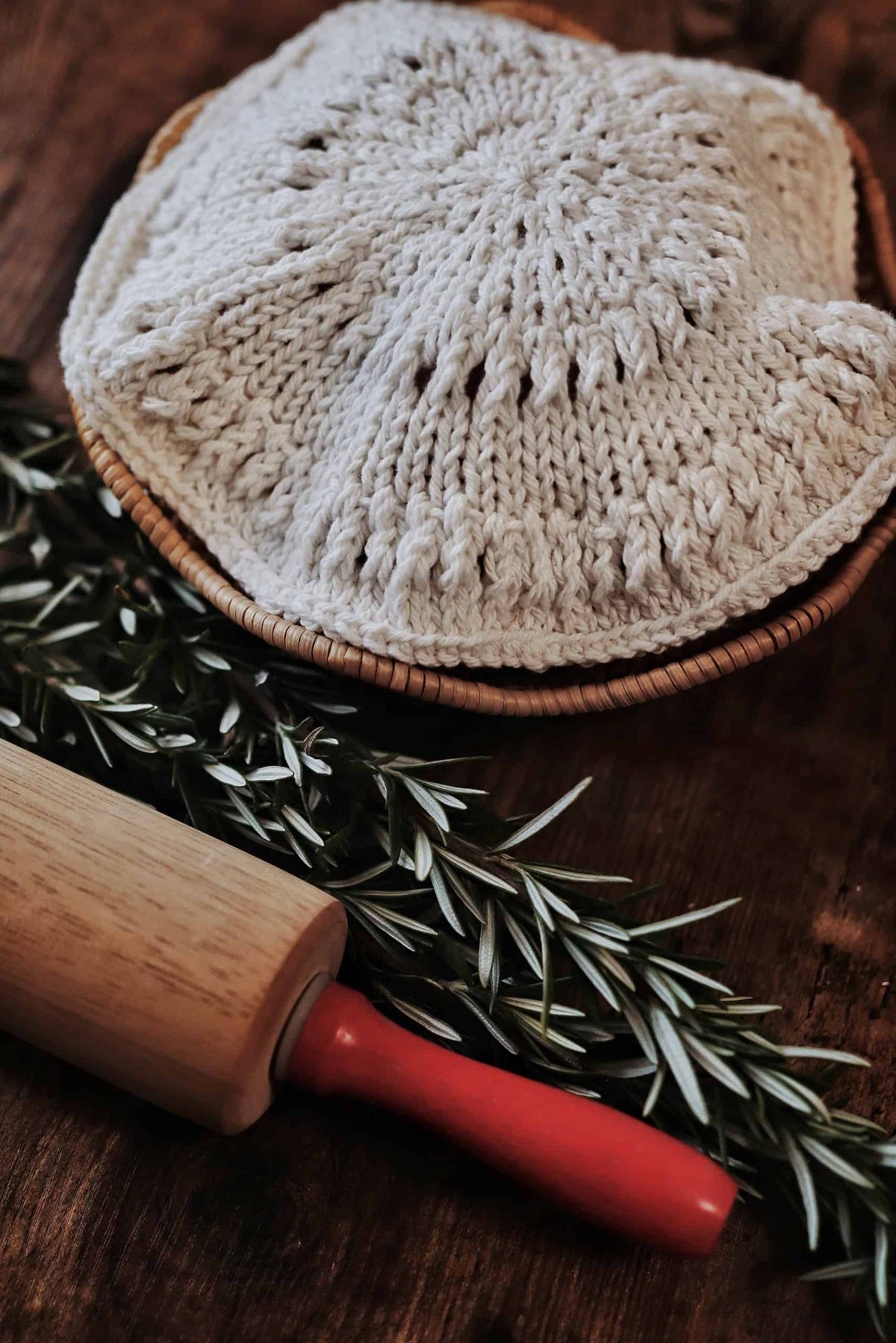Hand-knit bread warmer in cream yarn covering artisan loaf on rustic table setting