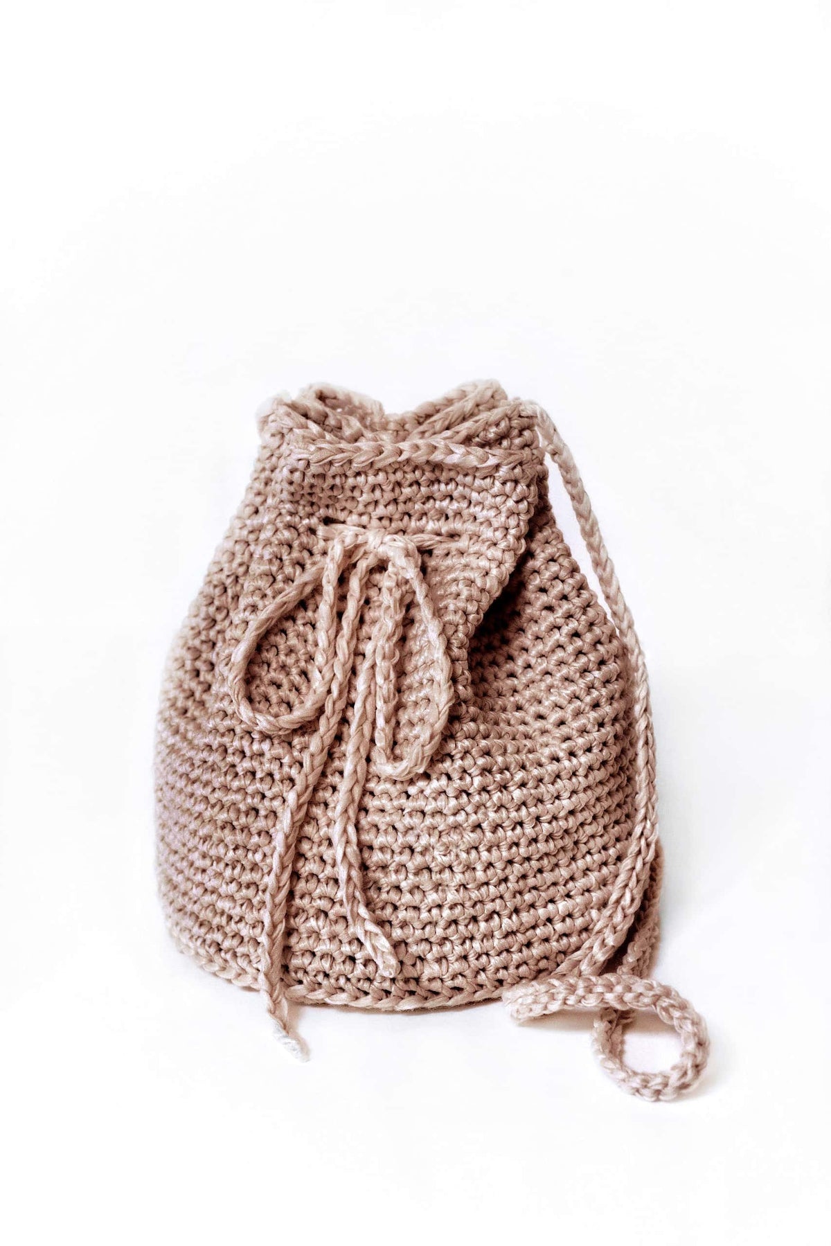 Cream bucket bag crochet pattern with drawstring closure and crossbody strap on wooden surface