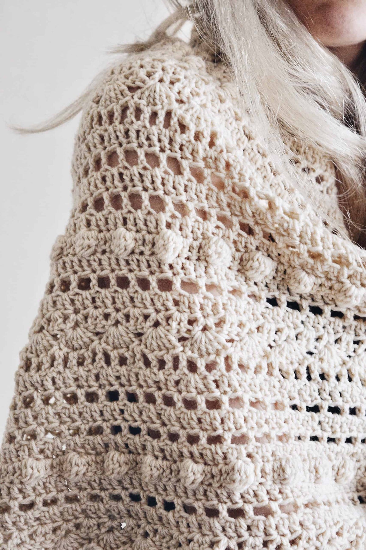Side view of cream triangle scarf showing intricate lace texture and bobble embellishments