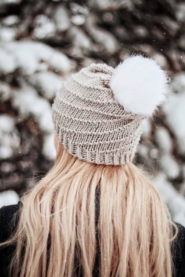 Woman wearing cream Iris beanie with spiral swirl design and faux fur pom pom