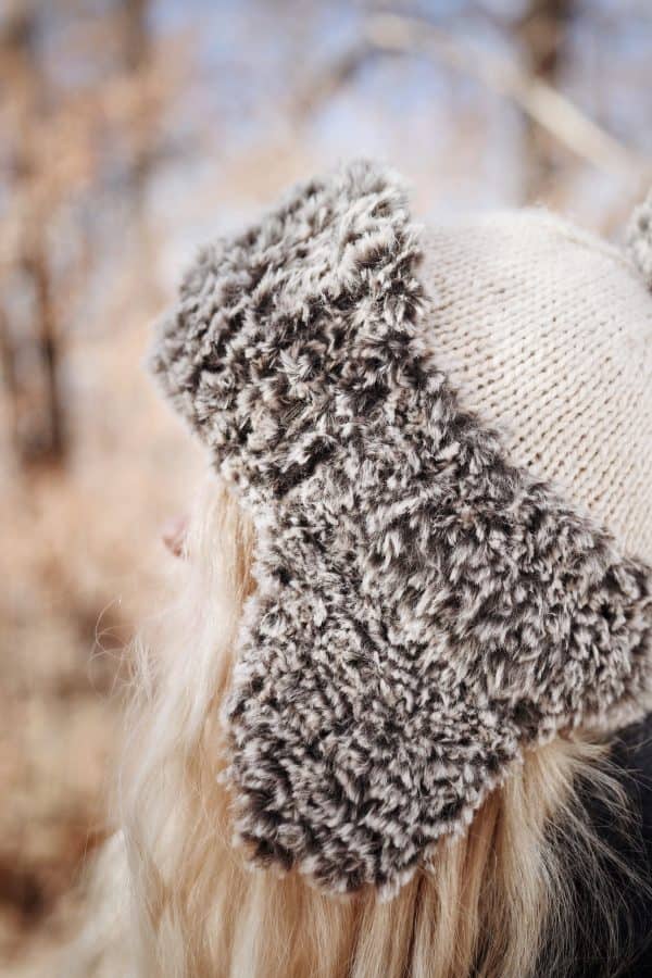 Back view of cream knit trapper hat with faux fur trim and earflaps - The Tundra Hat pattern