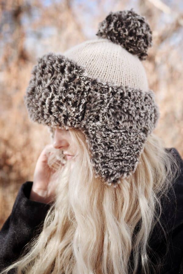 Woman wearing cream faux fur trapper hat with earflaps - The Tundra Hat knitting pattern by Darling Jadore