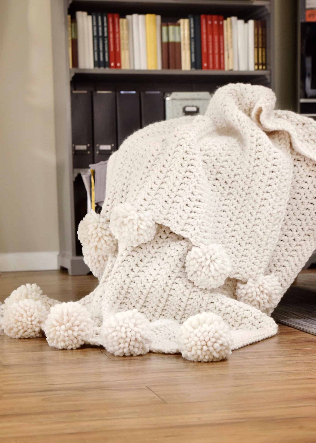 Bulky crochet throw blanket with pom pom trim folded to show texture and weight