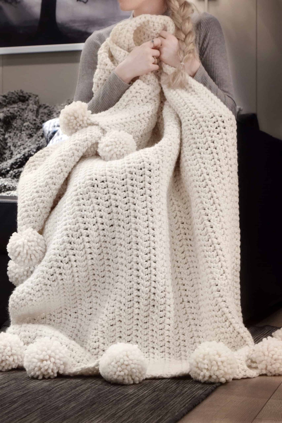 Handmade chunky crochet blanket with decorative pom poms displayed in modern hygge inspired home