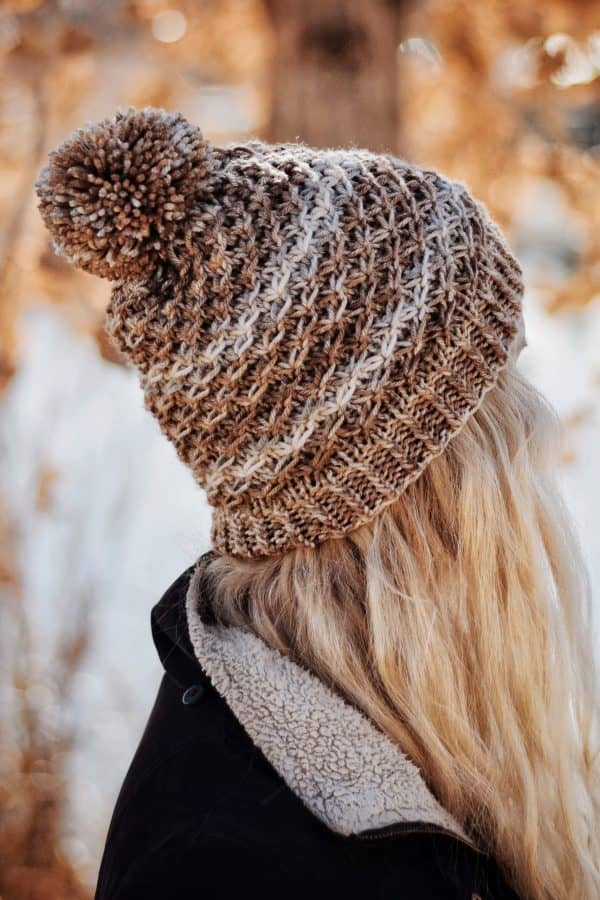 Textured beanie knitting pattern with ribbed brim and pom pom detail shown on model