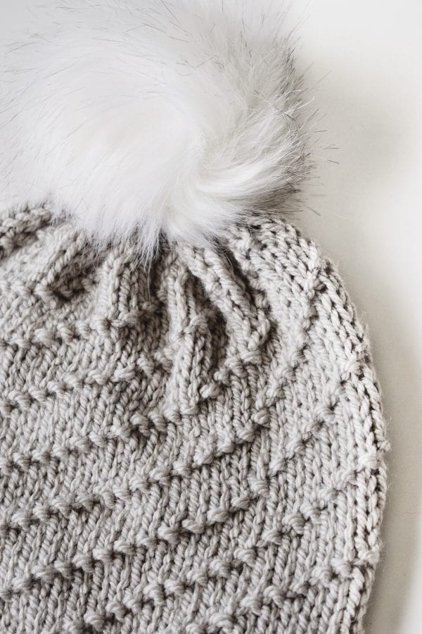 Side view of cream spiral beanie with ribbed brim and faux fur pom detail