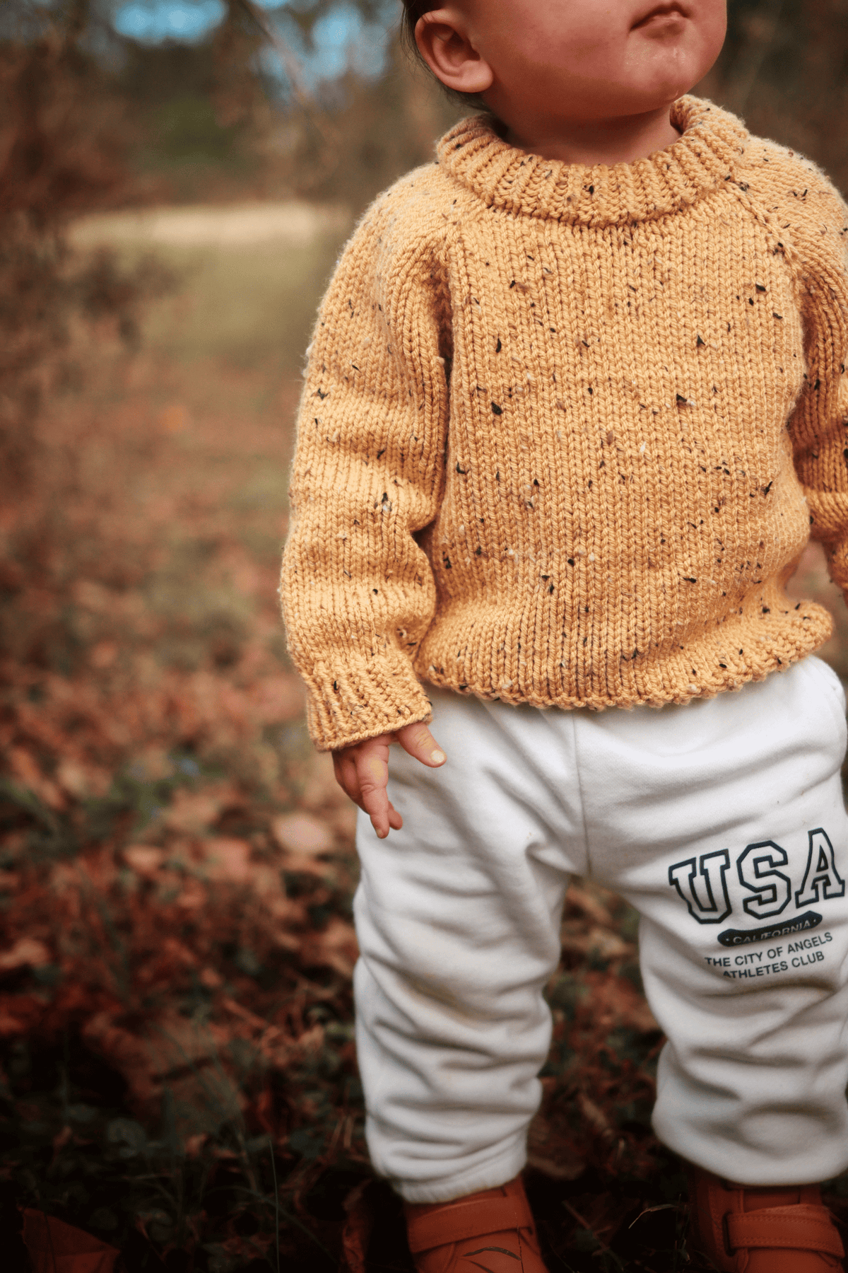 Back view of toddler wearing seamless raglan sweater knit in cream worsted yarn with classic fit
