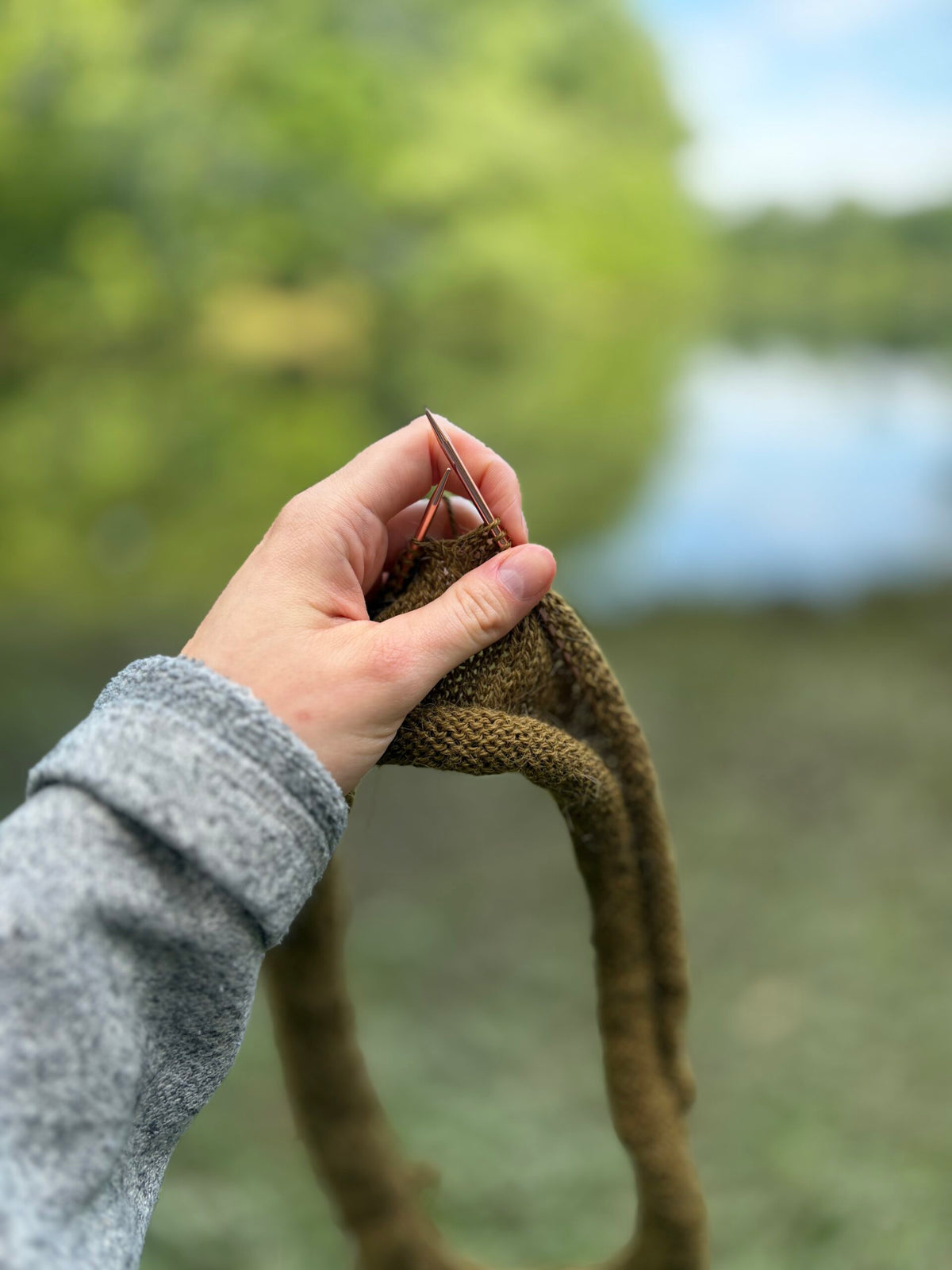 Olive camisole in progress on knitting needles by a lake - The Loft Camisole Knitting Pattern by Darling Jadore