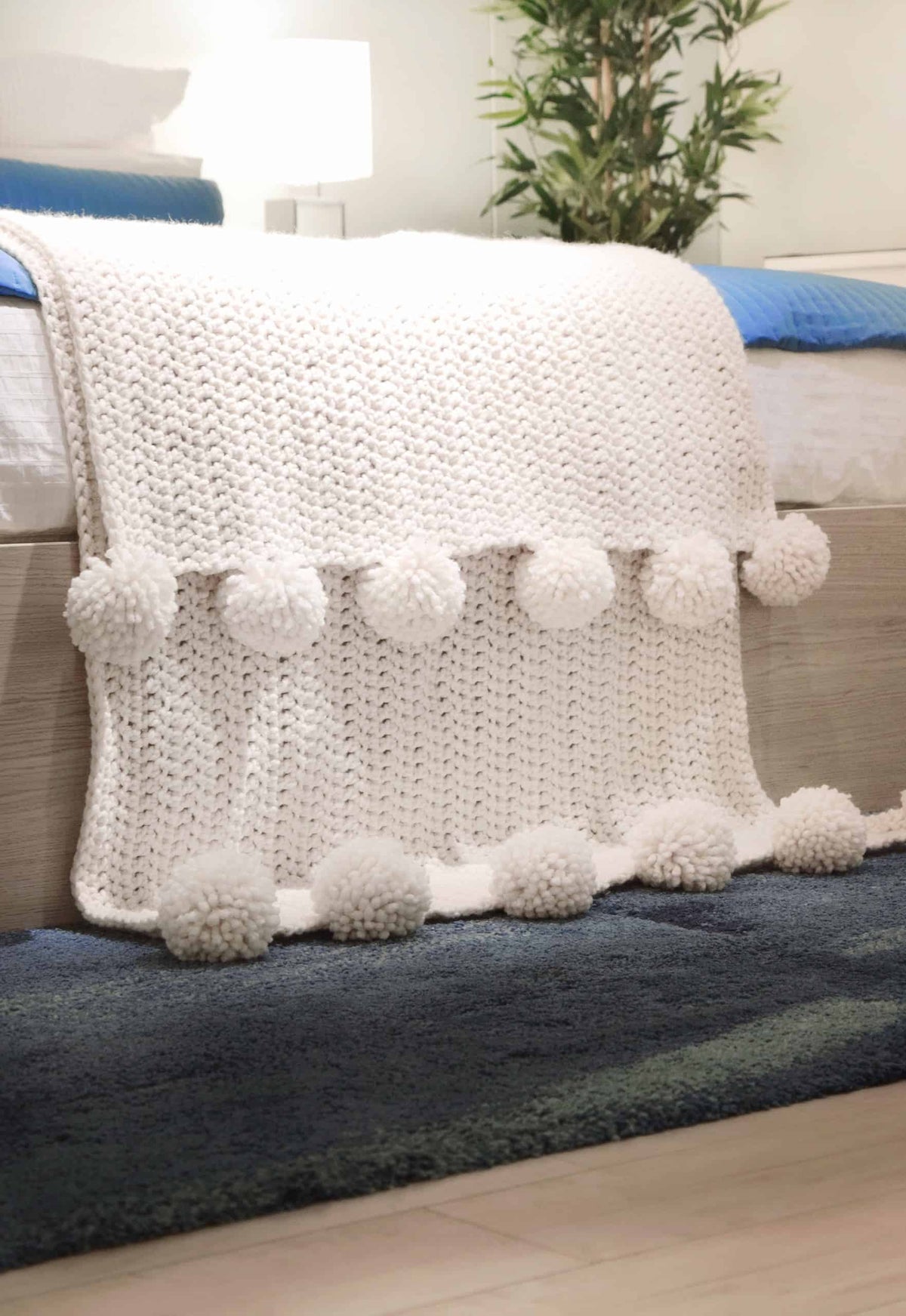 Close up of chunky crochet blanket texture showing simple beginner friendly stitches and pom pom details