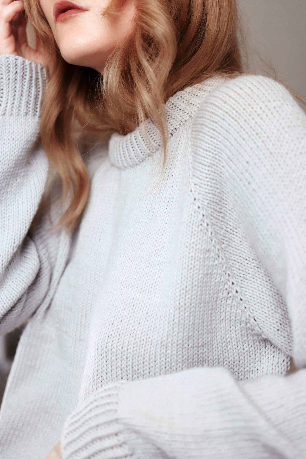 Woman wearing cream Essential Sweater knitting pattern with elegant double-knit neck and tapered sleeves