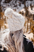 The Avalon cable knit beanie with pom pom in cream chunky yarn on wooden background