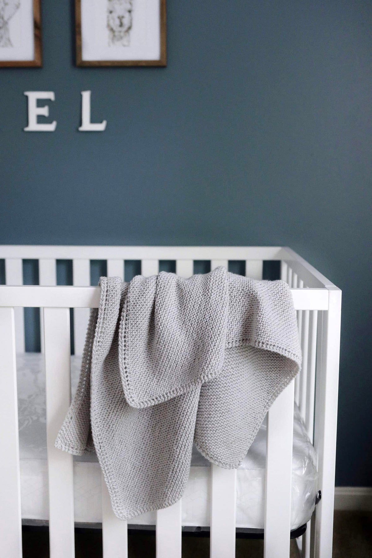 Cream knitted baby blanket with eyelet border draped over wooden chair - beginner knitting pattern