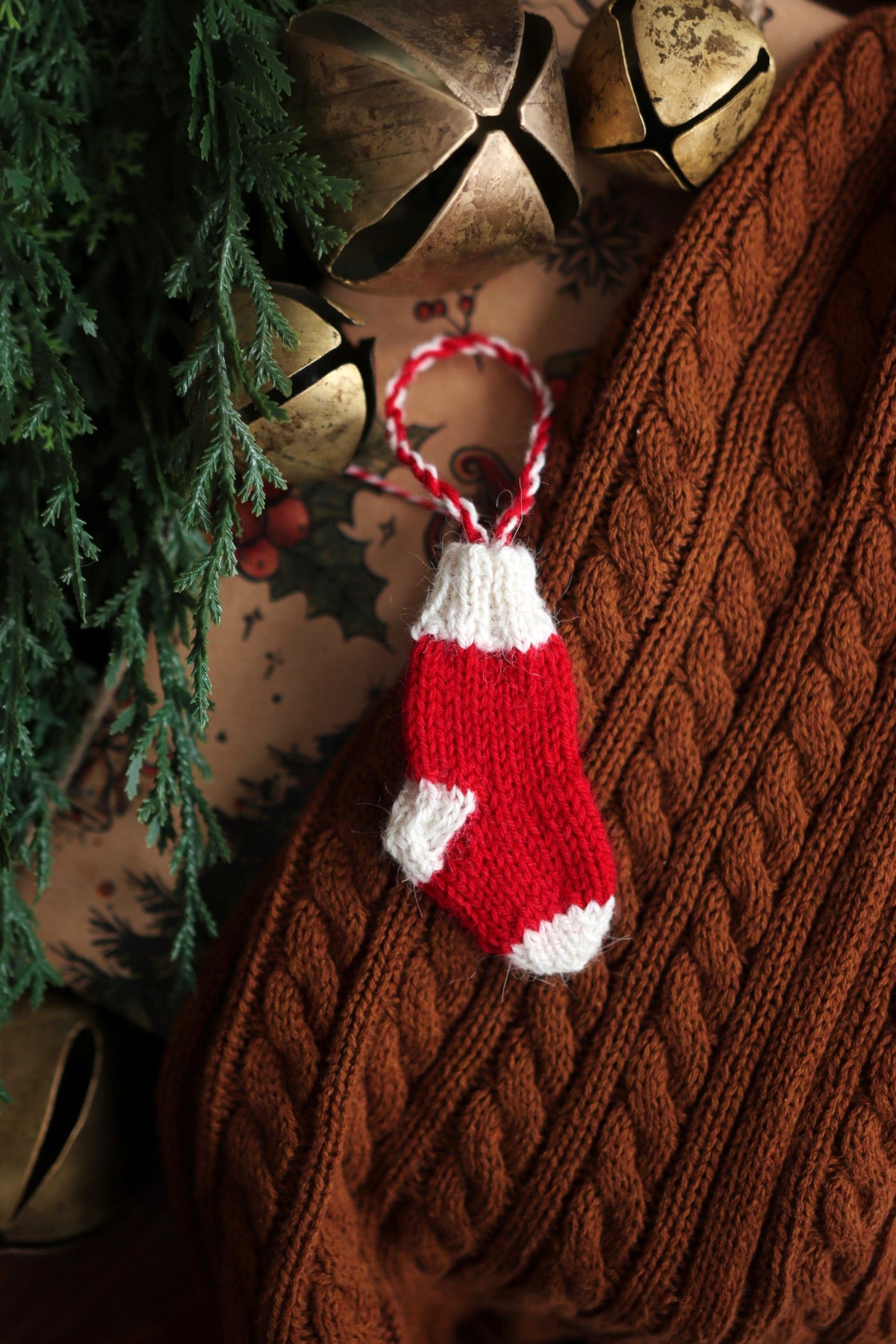 Knitted mini stocking ornament pattern displayed with holiday greenery and rustic Christmas decor