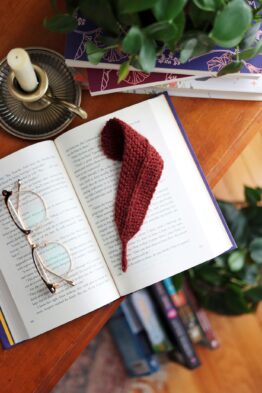 Delicate knitted feather bookmark in cream yarn on open book - beginner knitting pattern by Darling Jadore